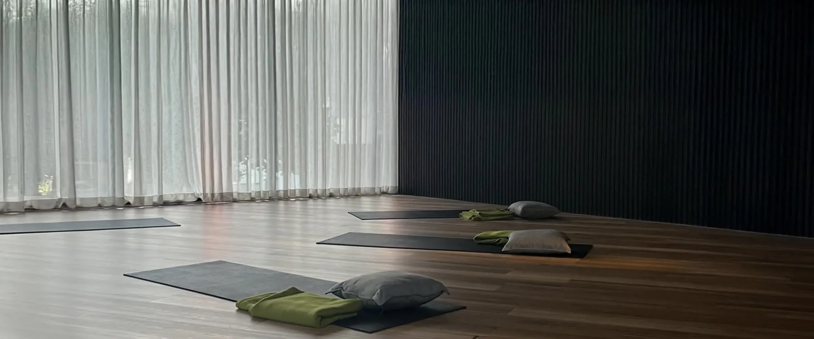 Mats and cushions laid out for a group breathwork class before tall sheer curtains