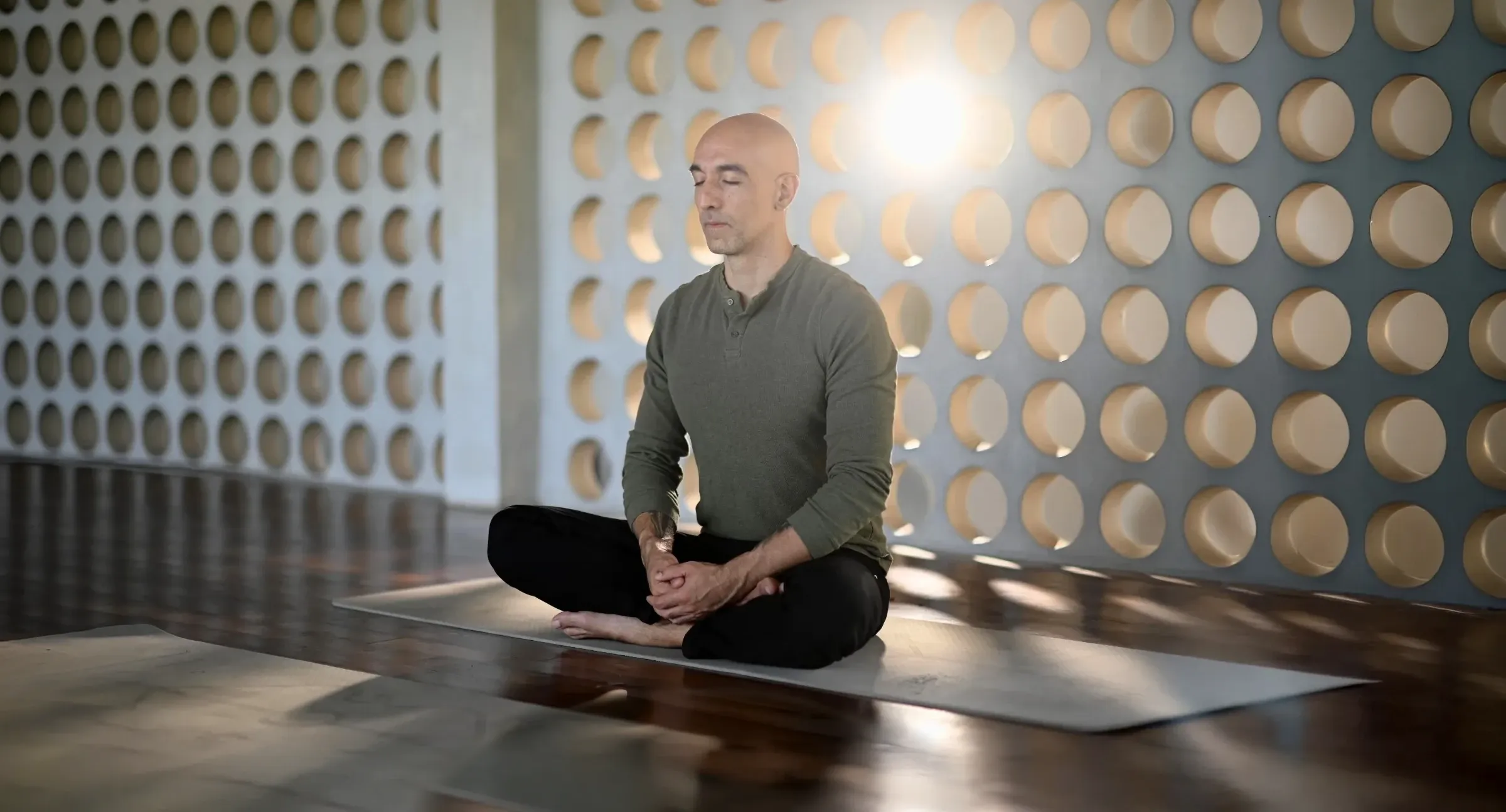 Mike McGregor seated cross legged on a mat, eyes closed, doing breathwork in a sunlit studio